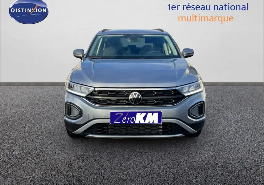 Vue frontale d'un Volkswagen T-Roc gris pyrite métal 2025 avec calandre noire et phares LED allumés.