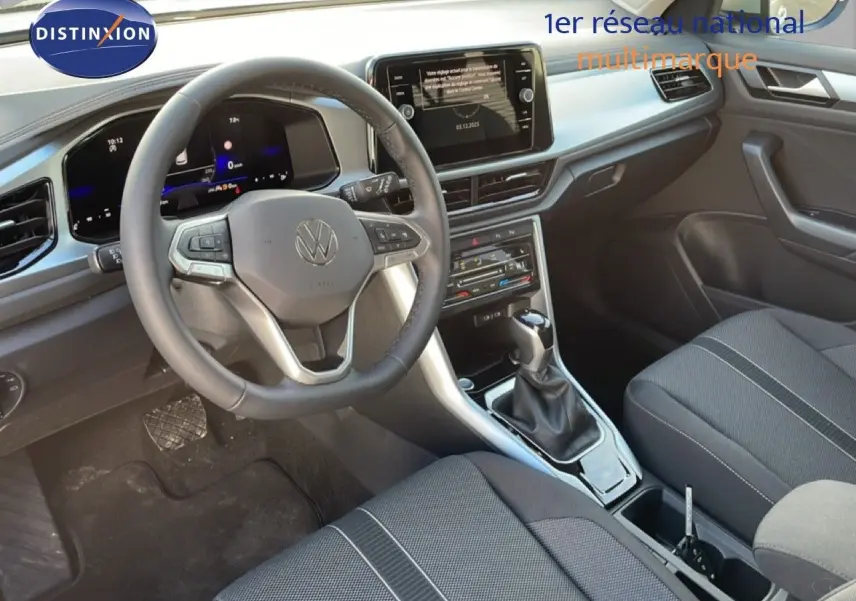 Vue intérieure du Volkswagen T-Roc 2025 montrant le volant, la console centrale avec boîte auto et les sièges en tissu noir.