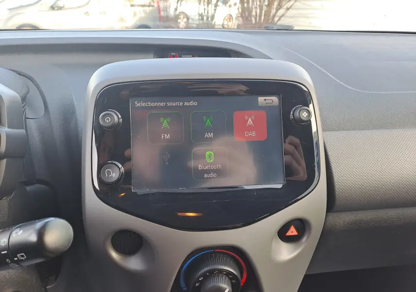 Vue rapprochée de l'écran tactile central du tableau de bord de la Peugeot 108 noire, affichant les options audio FM, AM, DAB et Bluetooth.