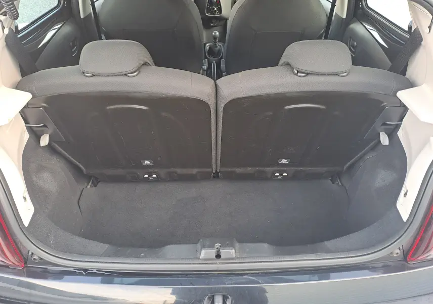 Coffre ouvert vu de l'arrière d'une Peugeot 108 noire, montrant les dossiers arrière et l'espace de chargement.