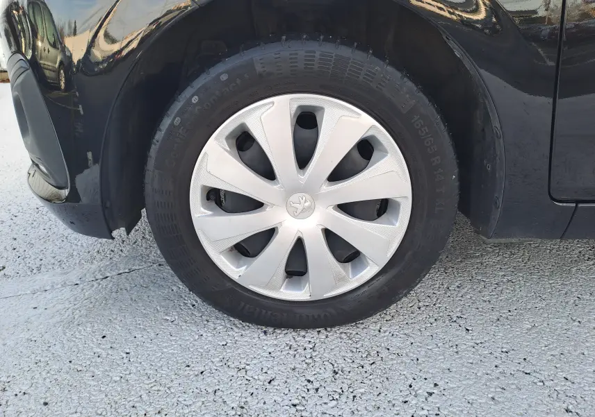 Gros plan sur la roue avant gauche noire d'une Peugeot 108 2020 avec enjoliveur argenté et logo lion central.