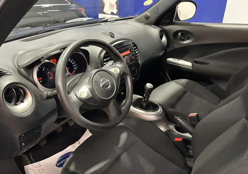 Vue intérieure côté conducteur du Nissan Juke noir métal 2012, volant cuir, tableau de bord et levier de vitesse manuel visibles.