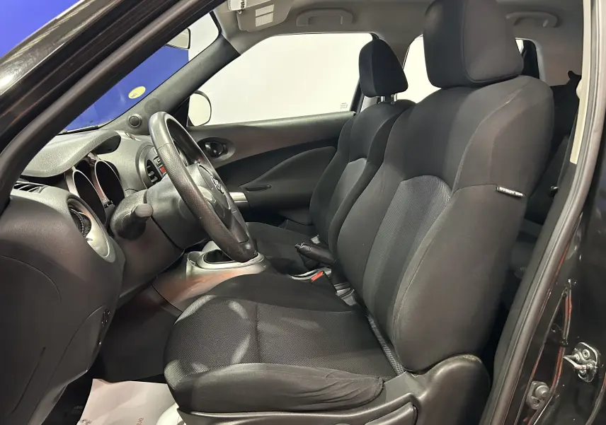Vue intérieure côté conducteur du Nissan Juke noir métal 2012, montrant les sièges avant en tissu noir et le volant cuir.