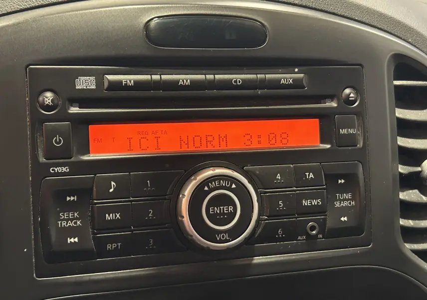 Gros plan sur la radio d’origine noire du Nissan Juke 2012 avec affichage digital orange allumé.