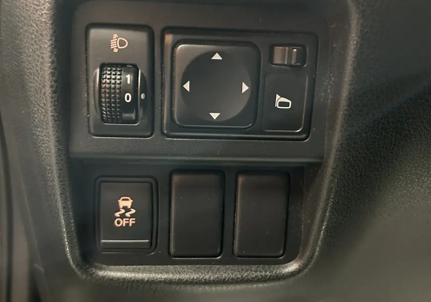 Gros plan sur les commandes noires du tableau de bord du Nissan Juke dci 110 Acenta, avec réglage des rétroviseurs et contrôle de stabilité.