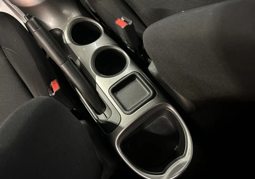 Vue rapprochée de la console centrale noire du Nissan Juke dci 110 Acenta, avec frein à main et porte-gobelets.