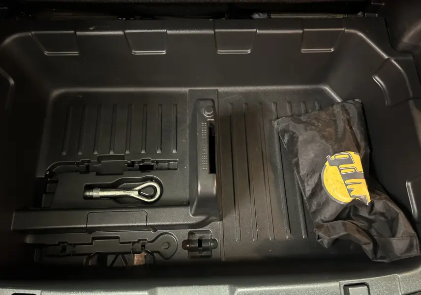 Coffre ouvert du Nissan Juke noir métal, vue de dessus montrant un crochet d'attelage et une pochette noire.