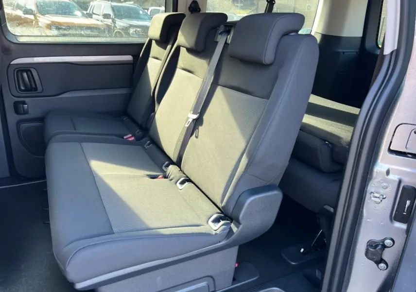 Vue intérieure côté droit du Peugeot Traveller gris acier 2025, montrant la banquette arrière trois places et la porte coulissante ouverte.