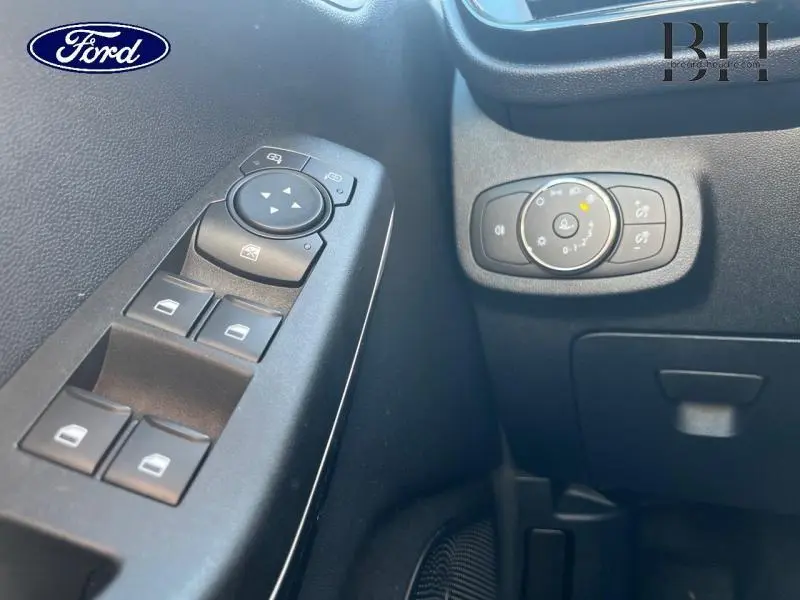 Détail intérieur côté gauche montrant les commandes des vitres électriques et le réglage des phares d’une Ford Fiesta bleu azur 2022.