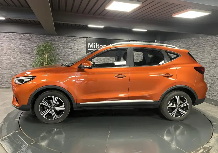 Profil côté gauche du SUV MG ZS orange métallisé 2022 avec jantes alliage 17 pouces dans un showroom.