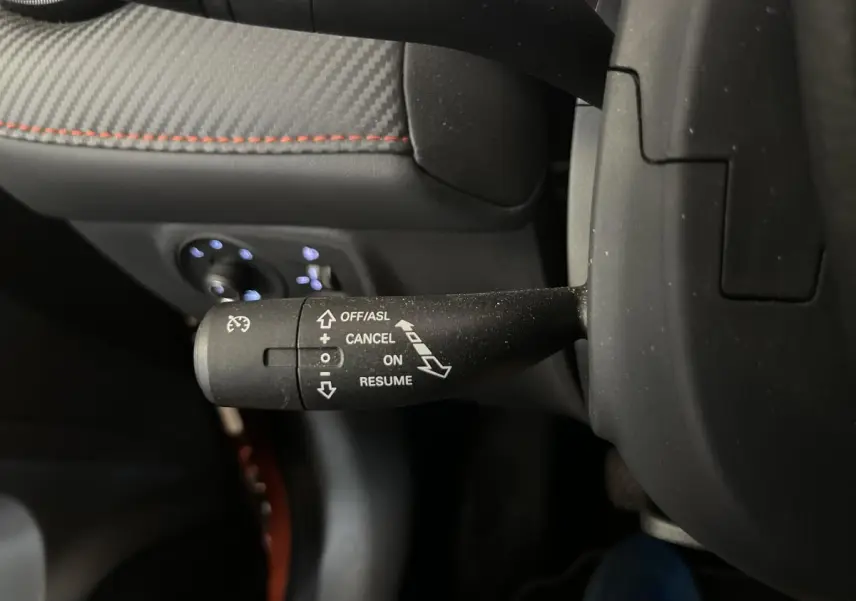 Gros plan sur la commande de régulateur de vitesse à gauche du volant dans l’habitacle noir et tissu du MG ZS orange.