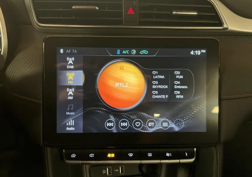 Écran tactile central allumé affichant la radio FM dans l'habitacle du MG ZS 1.5L Tech orange.