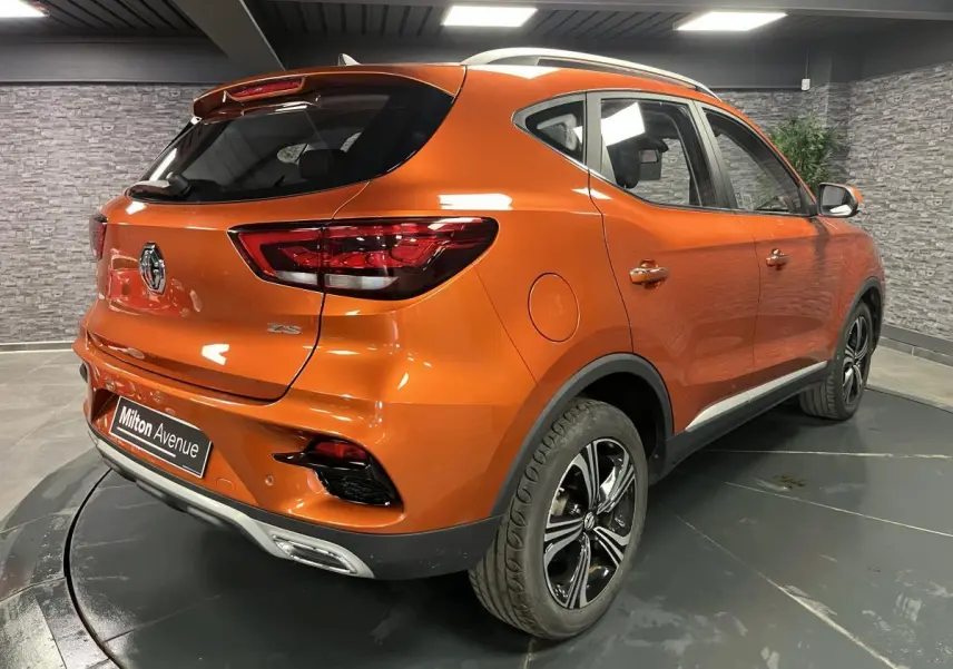 Vue 3/4 arrière droite d'un MG ZS orange métallisé 2022 avec jantes alliage et feux arrière LED dans un showroom.
