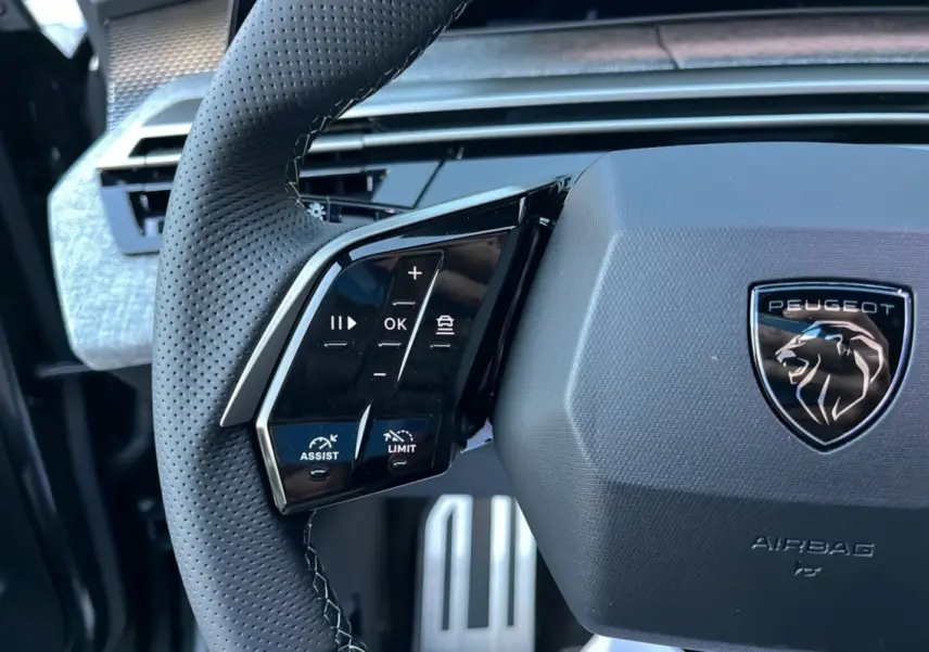 Gros plan sur le volant cuir perforé du Peugeot 5008 Hybrid 145 GT Alcantara avec commandes multifonctions et logo lion noir.