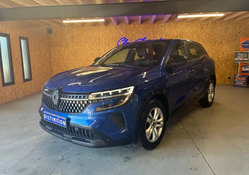 Renault Austral bleu en 3/4 avant droit dans un showroom, avec calandre distinctive et phares LED allumés.