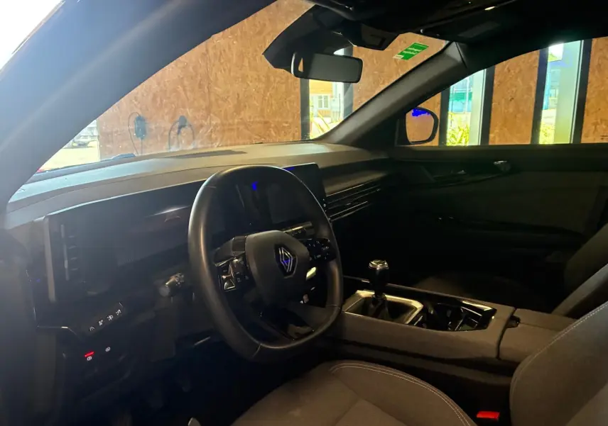 Intérieur du Renault Austral 2024 vu côté conducteur, avec volant multifonction, tableau de bord noir et levier de vitesse manuel.