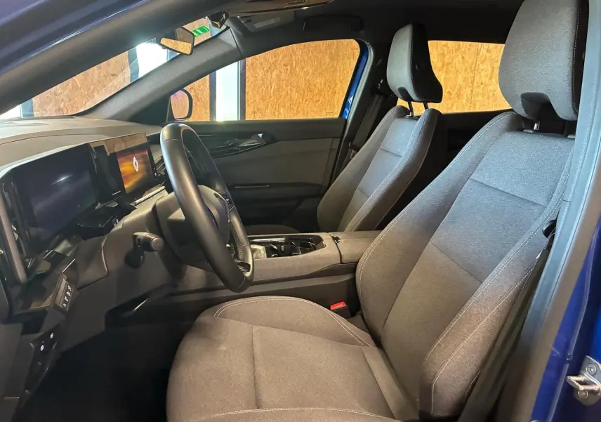 Vue intérieure côté conducteur du Renault Austral bleu 2024, sièges tissu gris et tableau de bord moderne avec écran digital.