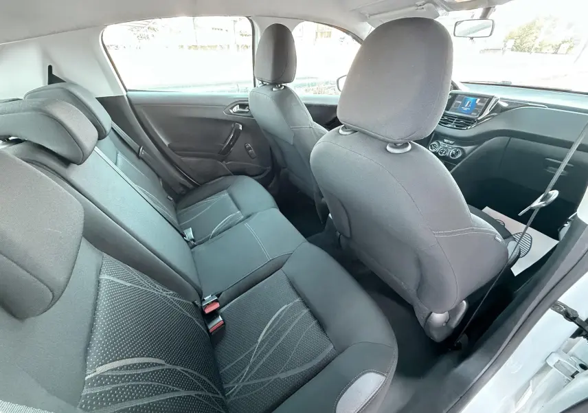 Vue intérieure arrière côté droit de la Peugeot 208 blanche de 2013, montrant les sièges noirs et la console avant.