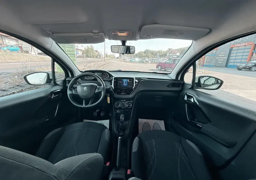 Vue intérieure avant du Peugeot 208 blanc de 2013, montrant le tableau de bord, volant et sièges noirs.