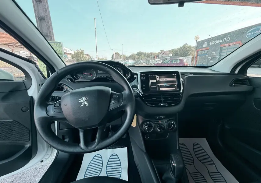 Vue intérieure avant de la Peugeot 208 blanche 2013, montrant le volant, tableau de bord et console centrale avec écran tactile.