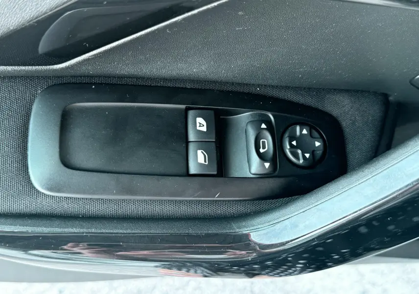 Gros plan sur les commandes de lève-vitres et réglage des rétroviseurs côté conducteur d'une Peugeot 208 blanche de 2013.