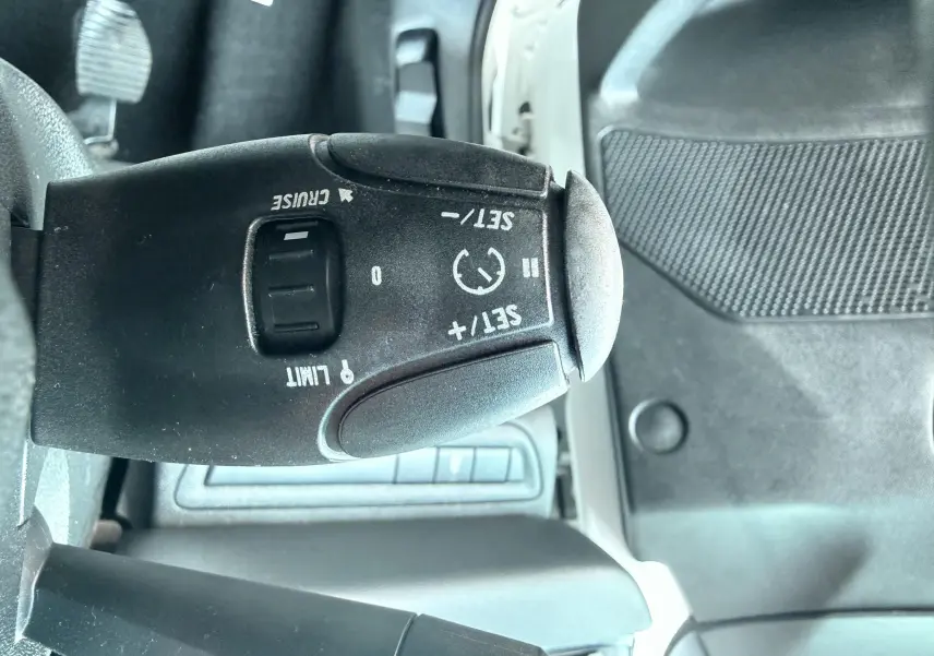 Gros plan sur la commande de régulateur de vitesse noire dans l’habitacle d’une Peugeot 208 blanche de 2013.