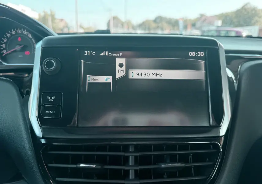 Écran central tactile du tableau de bord d’une Peugeot 208 blanche de 2013 affichant la radio FM à 94,30 MHz.