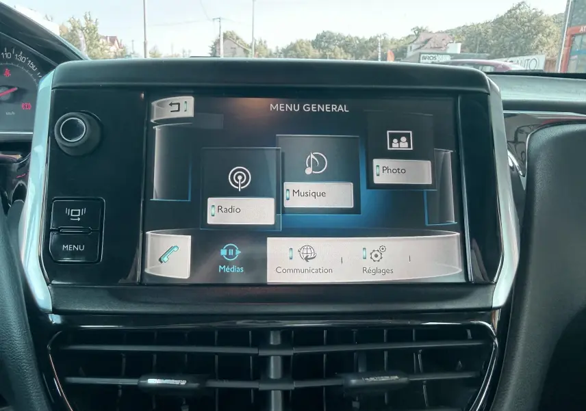 Vue rapprochée de l'écran tactile central du tableau de bord d'une Peugeot 208 blanche, affichant le menu général multimédia.
