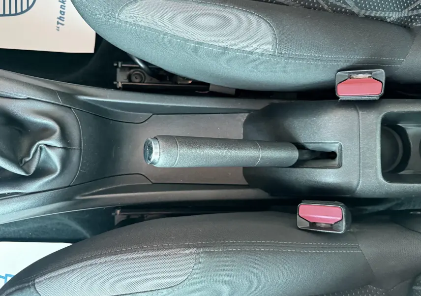 Vue plongeante sur le frein à main et la console centrale noire entre les sièges avant gris d'une Peugeot 208 blanche 2013.