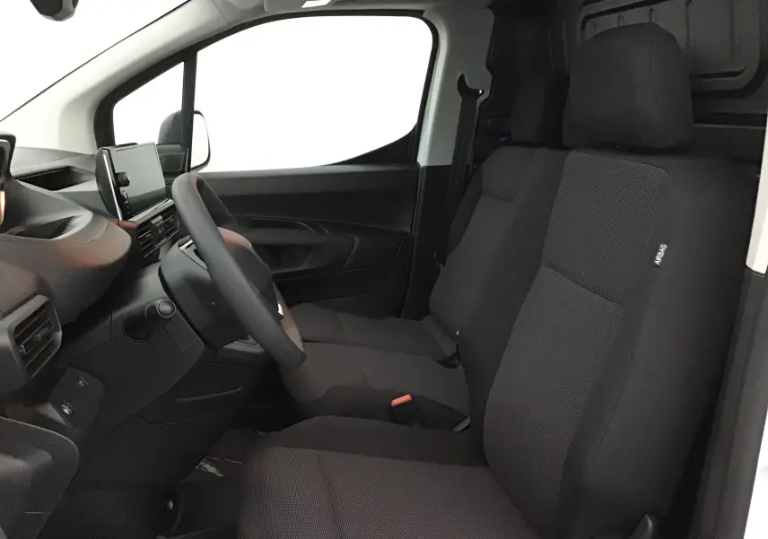 Vue intérieure côté conducteur du Peugeot Partner blanc, montrant les sièges avant en tissu noir et le tableau de bord moderne.