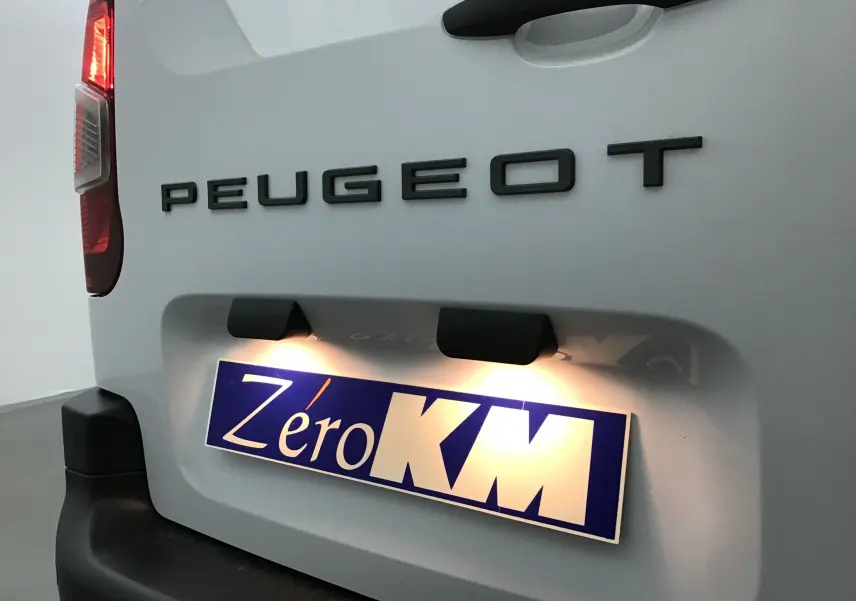 Gros plan arrière gauche du Peugeot Partner blanc montrant le logo et la plaque d'immatriculation éclairée "Zéro KM".