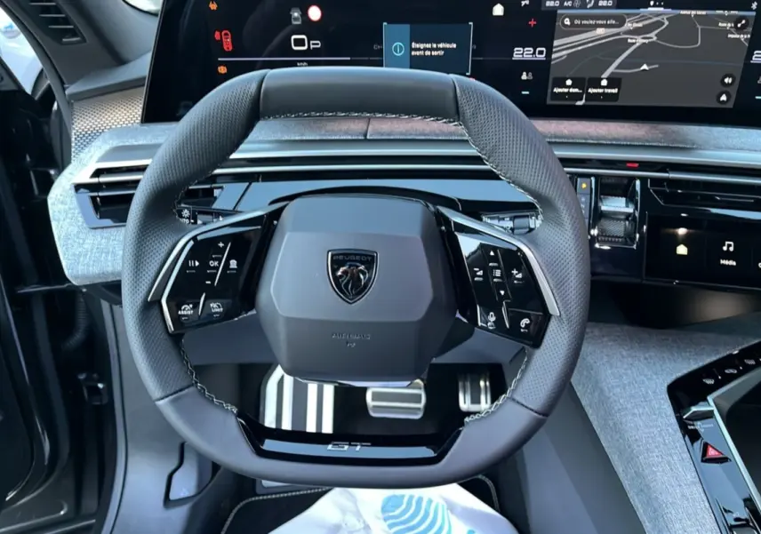 Vue rapprochée du volant cuir multifonctions Peugeot 5008 Hybrid GT 2025 avec tableau de bord numérique et finition Alcantara grise.