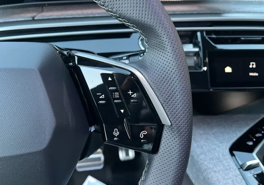 Gros plan sur la partie gauche du volant cuir perforé du Peugeot 5008 Hybrid 145 GT avec commandes multifonctions.