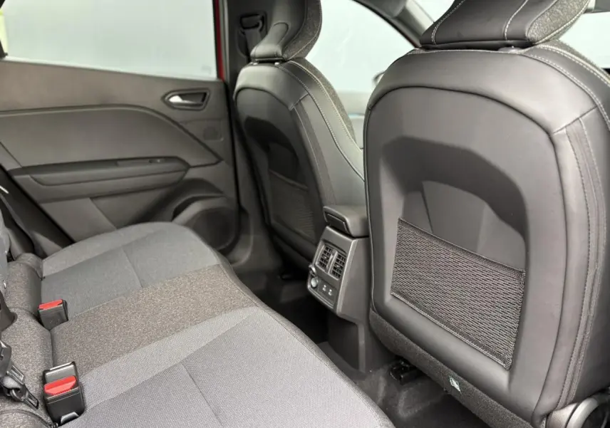 Vue intérieure arrière côté gauche du Renault Captur 2026, sièges tissu gris et dossiers avec filets de rangement.
