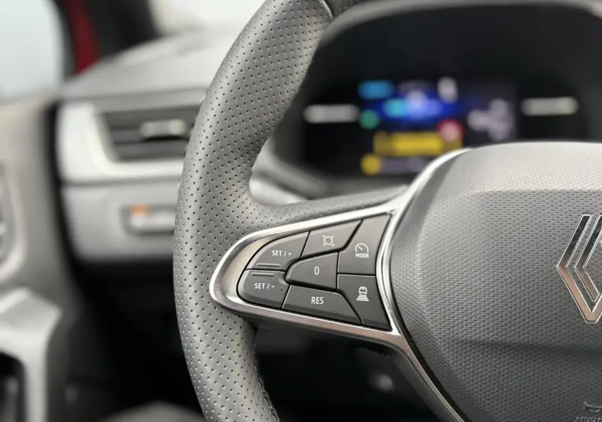 Gros plan sur le volant perforé côté gauche du Renault Captur rouge Flamme avec commandes intégrées et logo central.