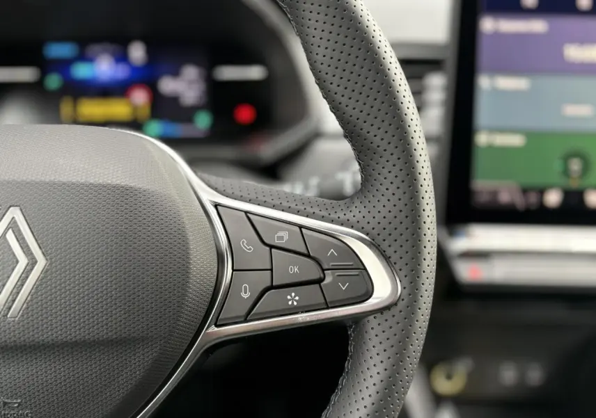 Gros plan sur le volant perforé noir avec commandes multifonctions du Renault Captur Rouge Flamme, tableau de bord flou en arrière-plan.