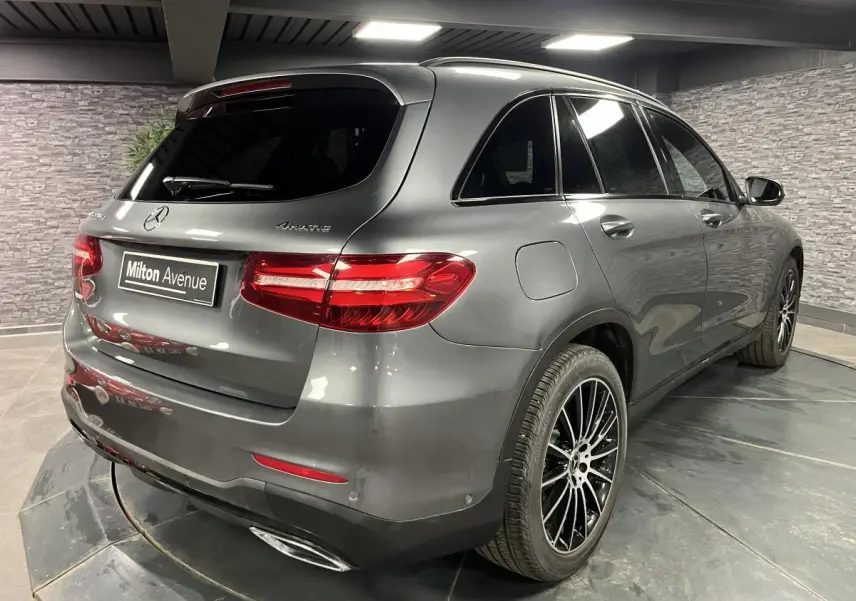 Vue 3/4 arrière droite d'un Mercedes GLC gris métallisé avec jantes AMG noires multibranches dans un garage.