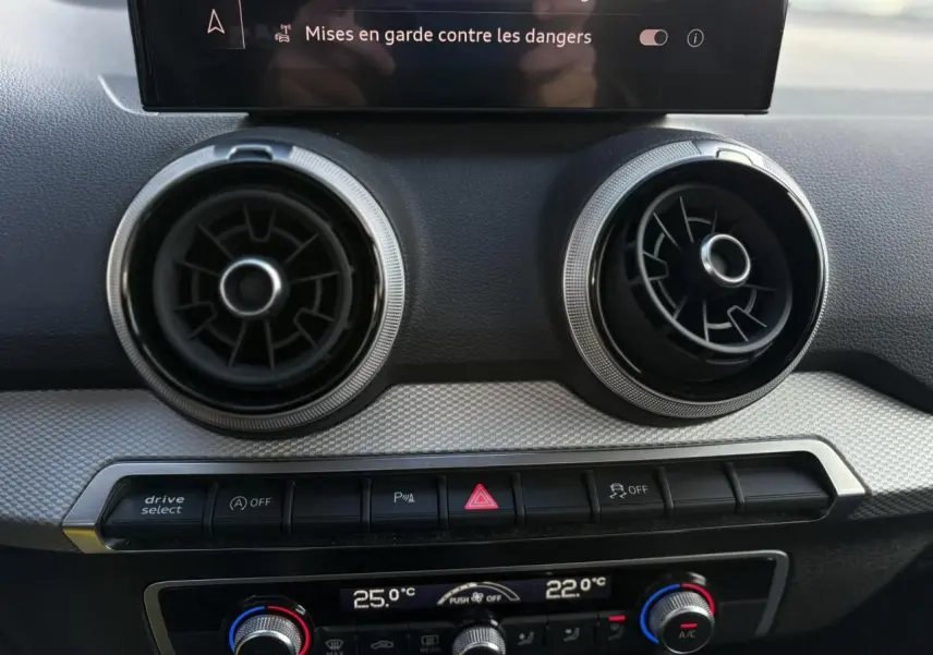 Détail du tableau de bord de l'Audi Q2 30 TDI S-Line 2025, montrant les aérateurs ronds et commandes de climatisation.
