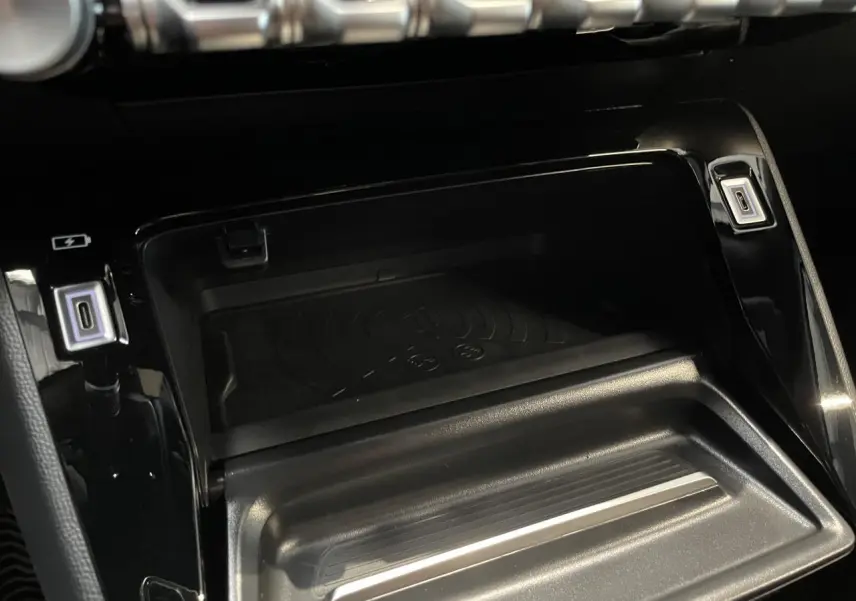 Gros plan sur la console centrale noire du Peugeot 2008 hybride 2026, avec zone de recharge sans fil et ports USB éclairés.