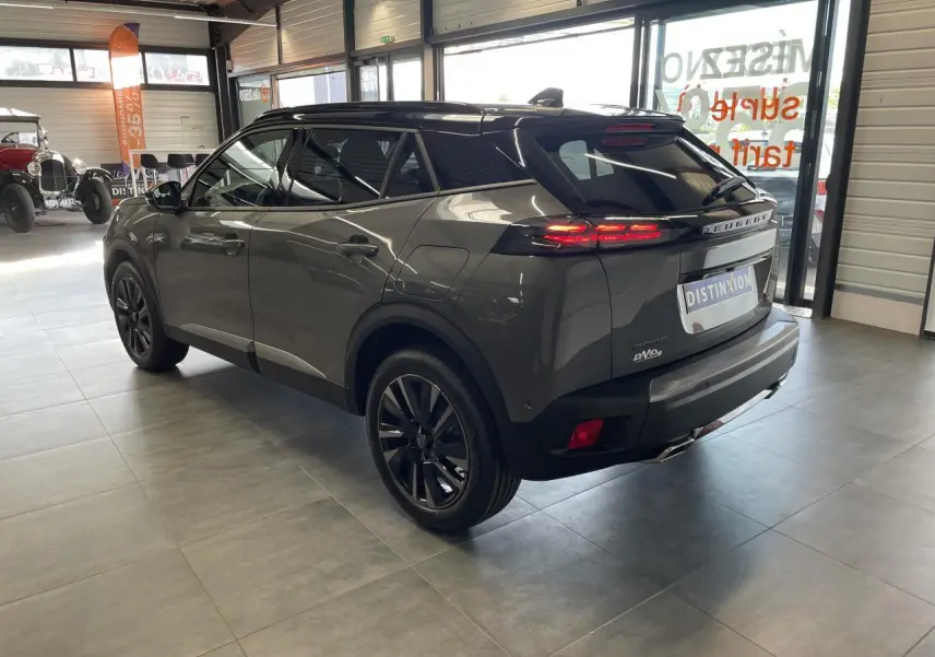 Vue 3/4 arrière droit d’un Peugeot 2008 gris hybride essence 2026 avec toit noir et jantes noires en showroom.
