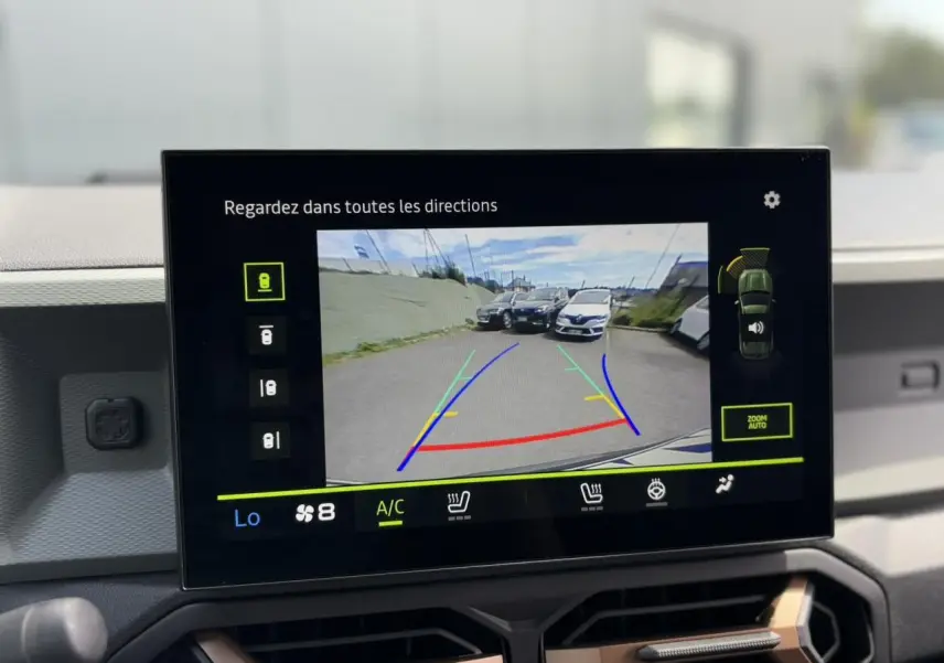 Écran tactile du Dacia Duster 2025 montrant la caméra de recul avec vue arrière sur un parking extérieur.