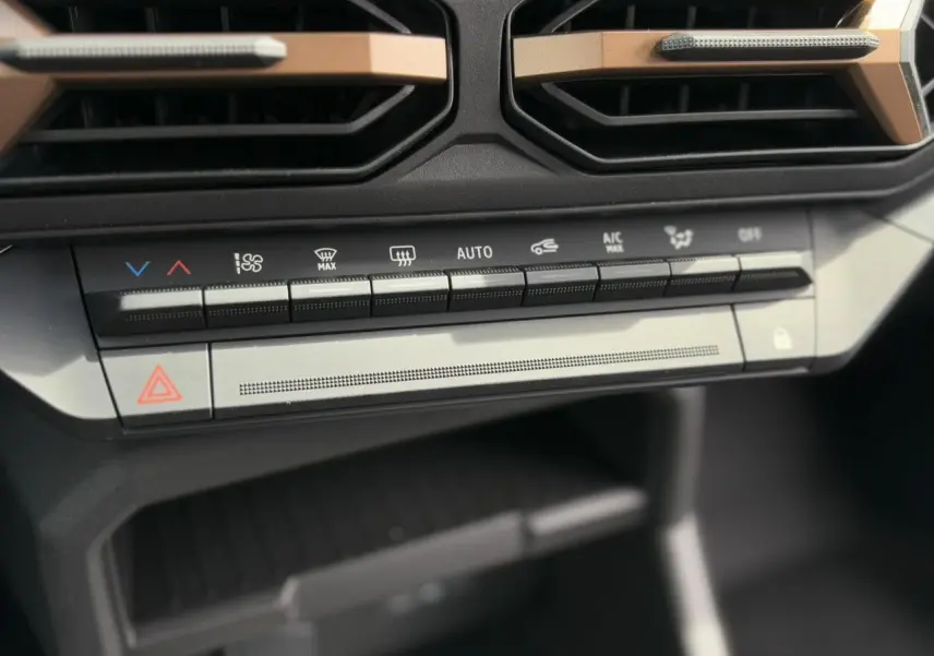 Détail de la console centrale du Dacia Duster 2025 gris Schiste, avec commandes climatisation et bouton d'alerte.