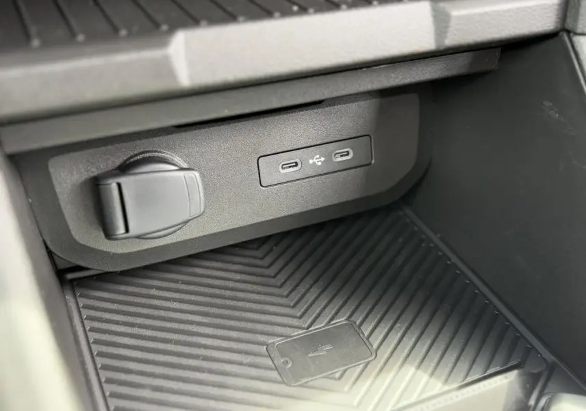 Gros plan sur la console centrale du Dacia Duster 2025 montrant les ports USB et la zone de charge sans fil.