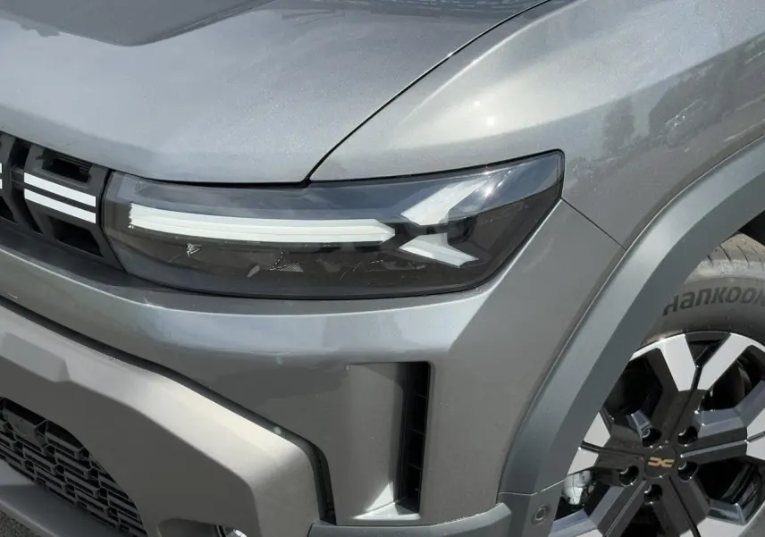 Gros plan sur l'avant droit du Dacia Duster gris schiste, mettant en valeur son phare LED et sa jante alliage noire et argentée.