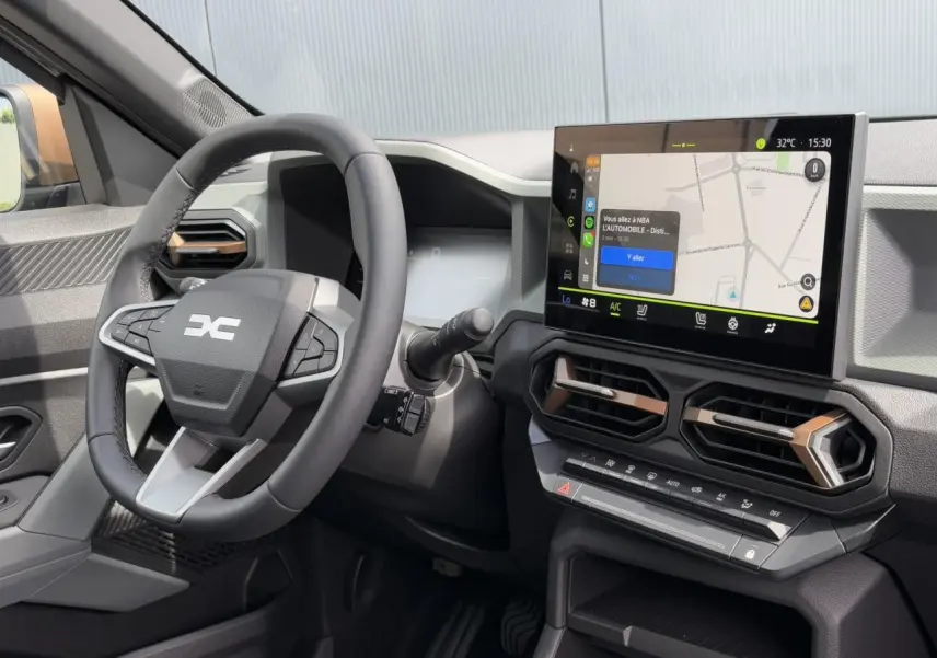 Vue intérieure du tableau de bord du Dacia Duster 2025 avec écran tactile GPS et volant multifonction noir.