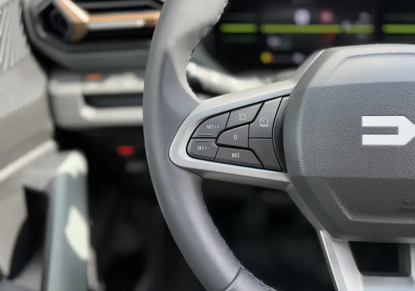 Gros plan sur le volant gris du Dacia Duster 2025 avec commandes intégrées et tableau de bord digital flou en arrière-plan