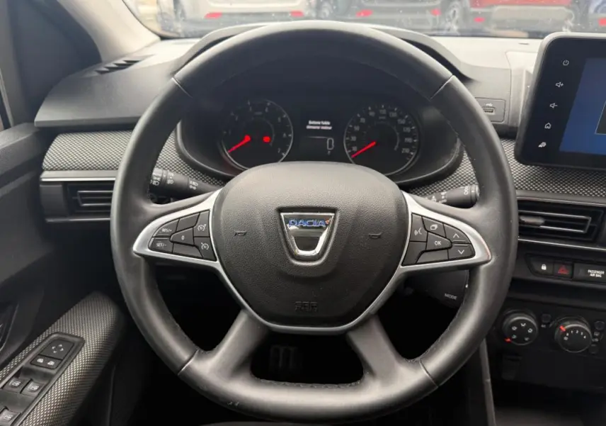 Vue rapprochée du volant noir du Dacia Sandero 2021 avec commandes intégrées et tableau de bord digital.