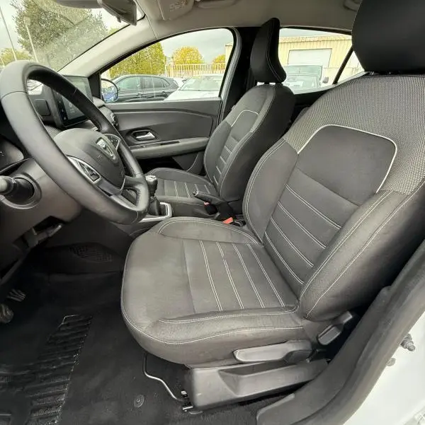 Vue intérieure côté conducteur de la Dacia Sandero blanche 2021, sièges noirs avec surpiqûres claires et volant réglable.