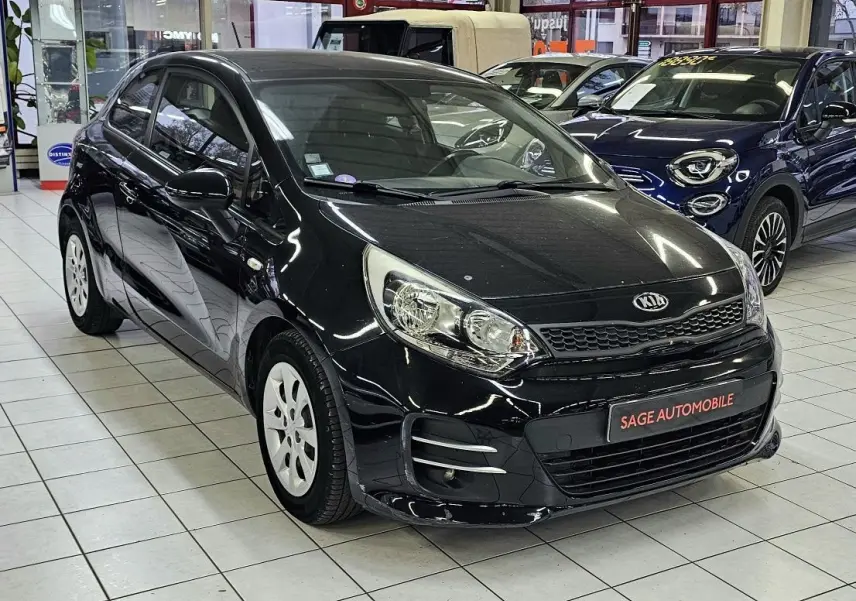 KIA RIO III noire vue 3/4 avant droit en showroom, avec jantes blanches et calandre caractéristique.