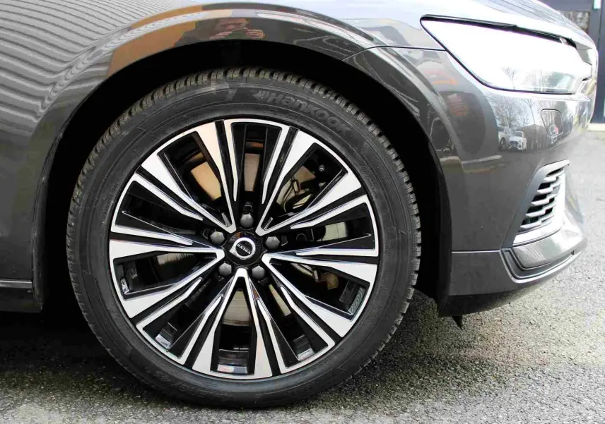 Gros plan sur la roue avant droite d'une Volvo S60 2024 gris métal, avec jante alliage noir et argentée distinctive.